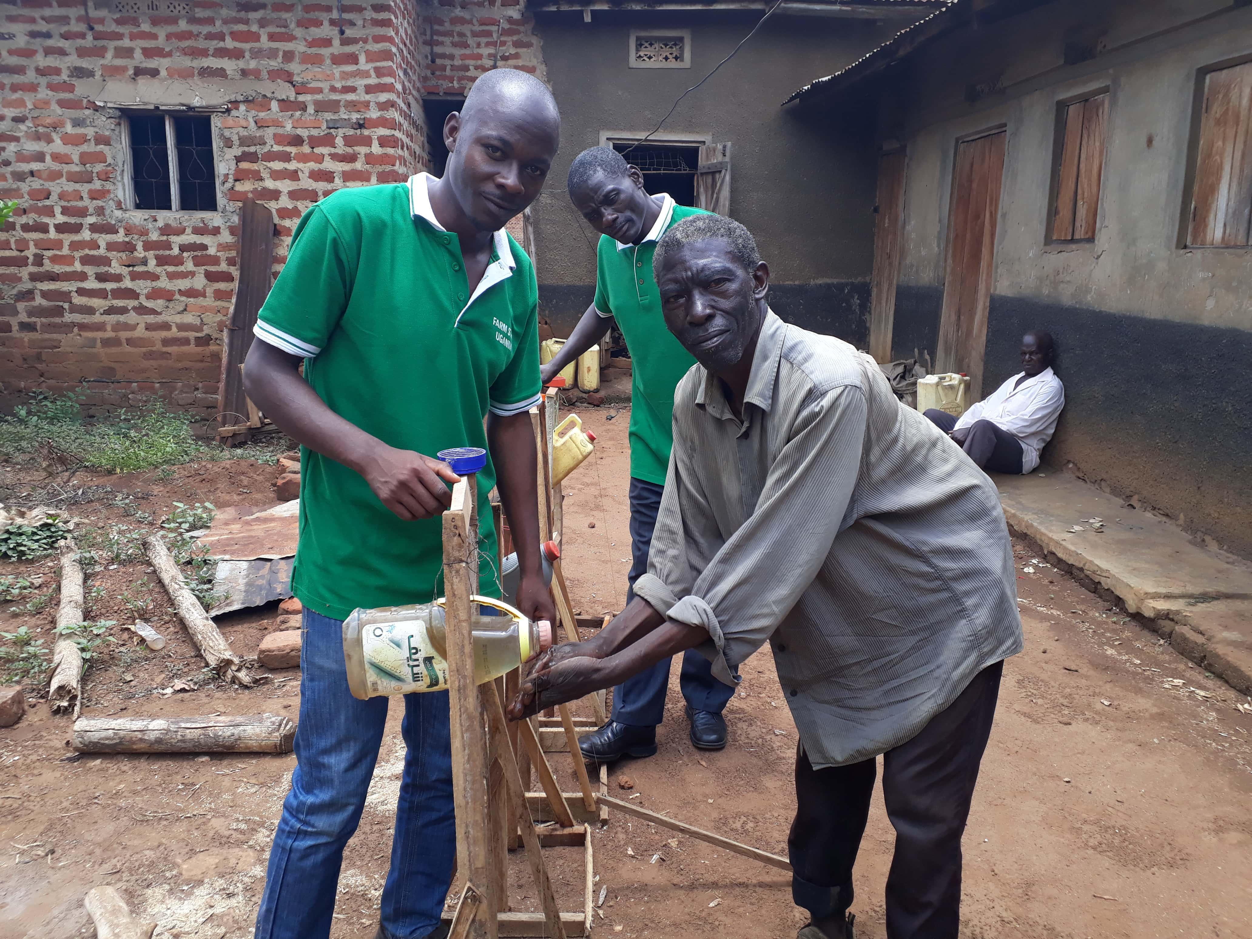 In Uganda, Mudoola with FARM STEW trainers Daniel and Steven, demonstrating how his mobile tippy-tap works. [Photo: FARM STEW]