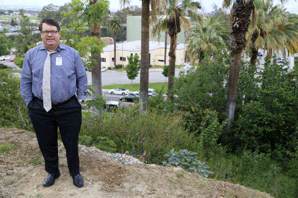 Larry Kidder, writer and editor for public relations at Loma Linda University Health, standing at the top of the hill where the stairs once ended. The nearby trees once lined the stairs, while the parking lot below is the site of the former train station. (Susan Onuma / LLUH)