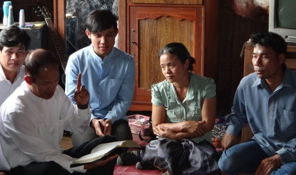 Buonaparte Vannadee, left, president of the Adventist Church in Laos,  studying the Bible with the man who was delivered from the spirit in the hospital, right, and his family. (Laos Field)