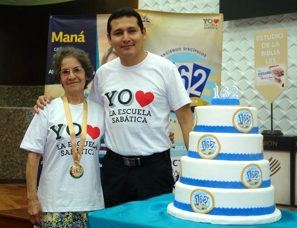 Loida Pinedo Dávila posing with former student Omar Bullón, stewardship ministries director for the Adventist Church in north Peru, near a cake celebrating Sabbath School's 162nd anniversary. (SAD)