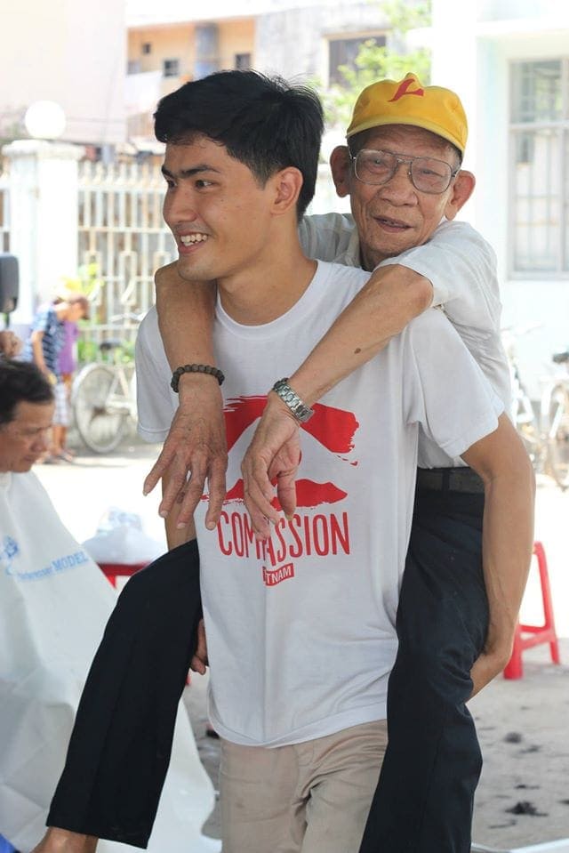 A One Year in Mission volunteer carrying an elderly man to a free health day event in Phuoc Binh Ward, District 9, of Ho Chi Minh City, Vietnam. (Keiko Le / SSD)