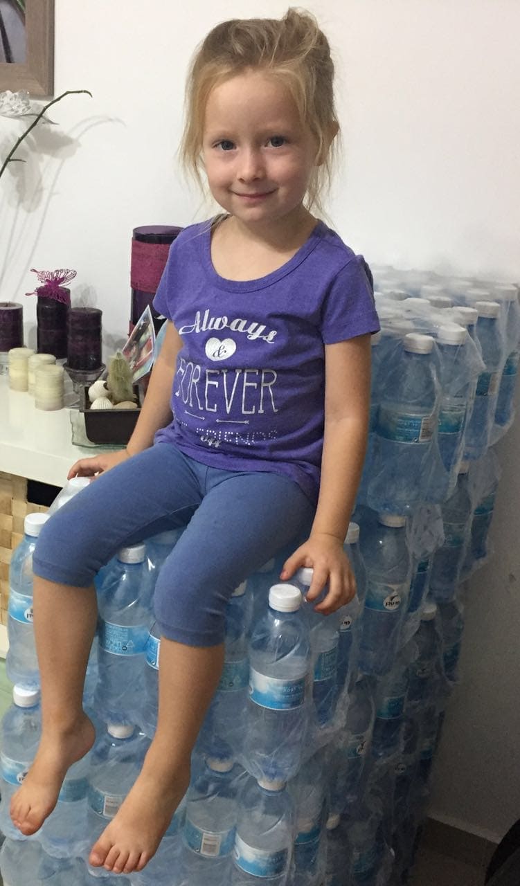A girl sitting on a pile of water bottles that Adventist young people plan to distribute for free to sunbathers on a beach in Tel Aviv, Israel, this weekend together with the printed verse: “I am the Alpha and the Omega, the Beginning and the End. To the thirsty I will give water without cost from the spring of the water of life” (Revelation 21:6). (Sara Cassal)