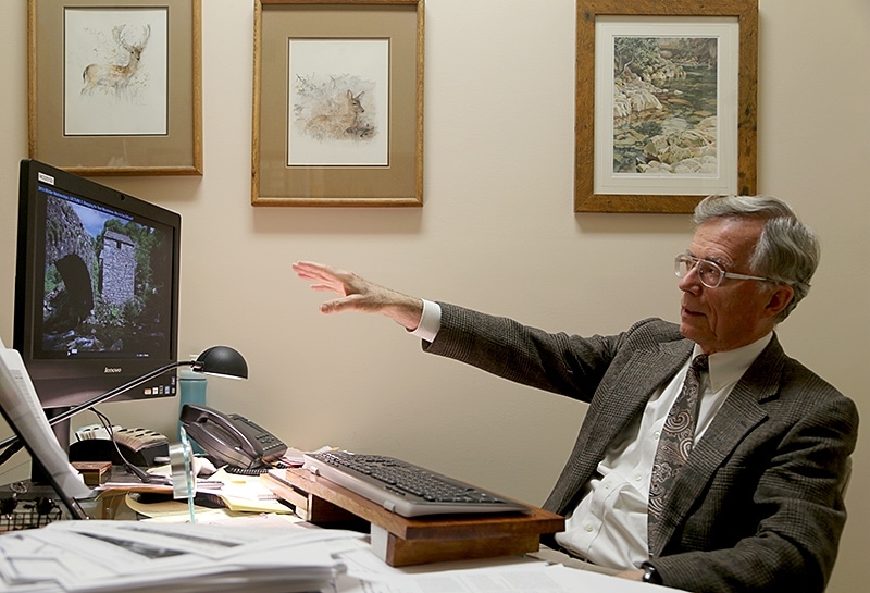 Brian Bull, MD, points to a photo of the stone mill in England where he learned an important secret about gastrointestinal health. The painting above his head depicts the stream that powers the mill. (LLU photo)