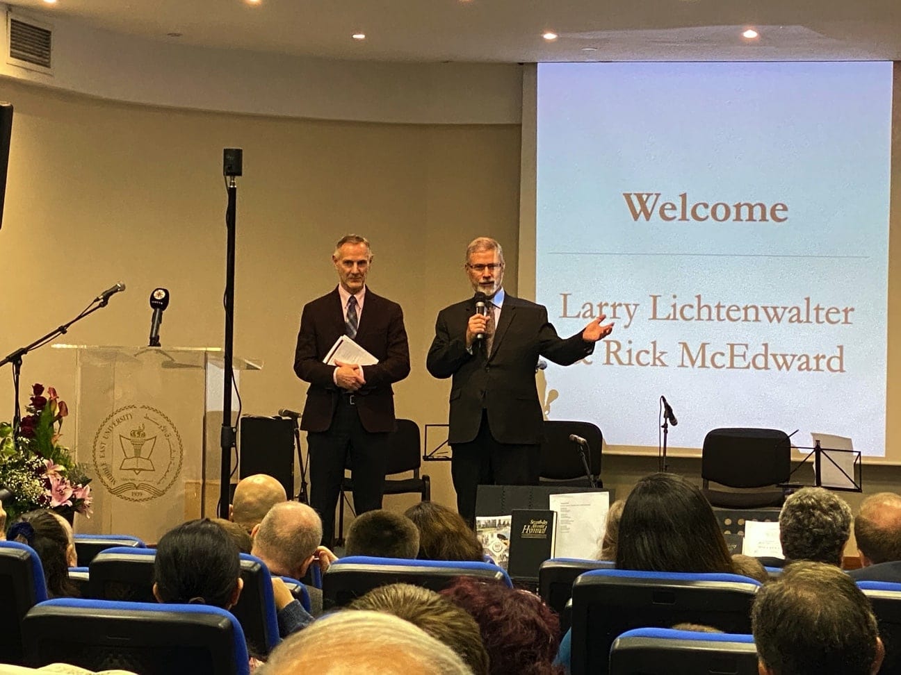 Rick McEdward (right), chairman of the Middle East University (MEU) board and president of the Middle East and North Africa Union church region, addresses the group gathered to celebrate the 80th anniversary of the school. By his side is current MEU president Larry Lichtenwalter. [Photo: Middle East University Communication]