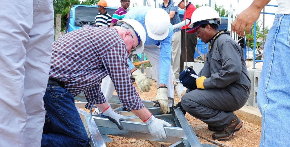 Wilson, center, gives Blasious Ruguri, right, president of the East-Central Africa Division, a lesson on how to build with a cordless drill. General Conference general vice president Lowell Cooper is to the left. Photo: Libna Stevens / IAD