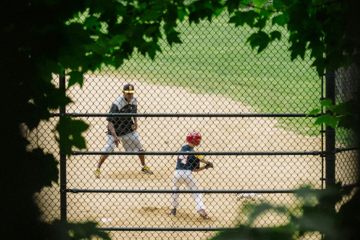 A child prepares to bat on a baseball field while a parent stands nearby offering guidance.