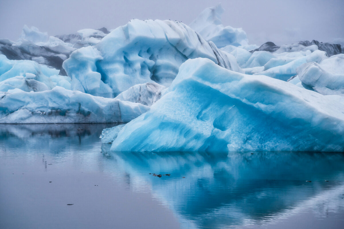 Glacial ice drifts silently across a still lagoon, its smooth reflection visible in the clear water below.