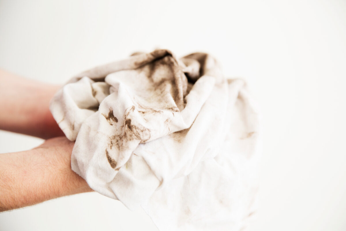 Hands hold a dirty, stained cloth against a plain background