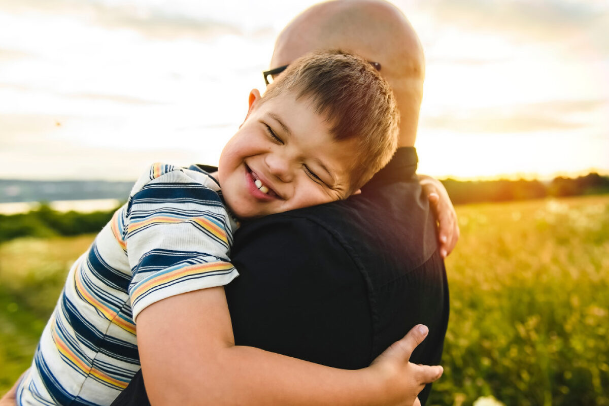 A smiling child hugs a parent tightly in a warm, sunlit field.