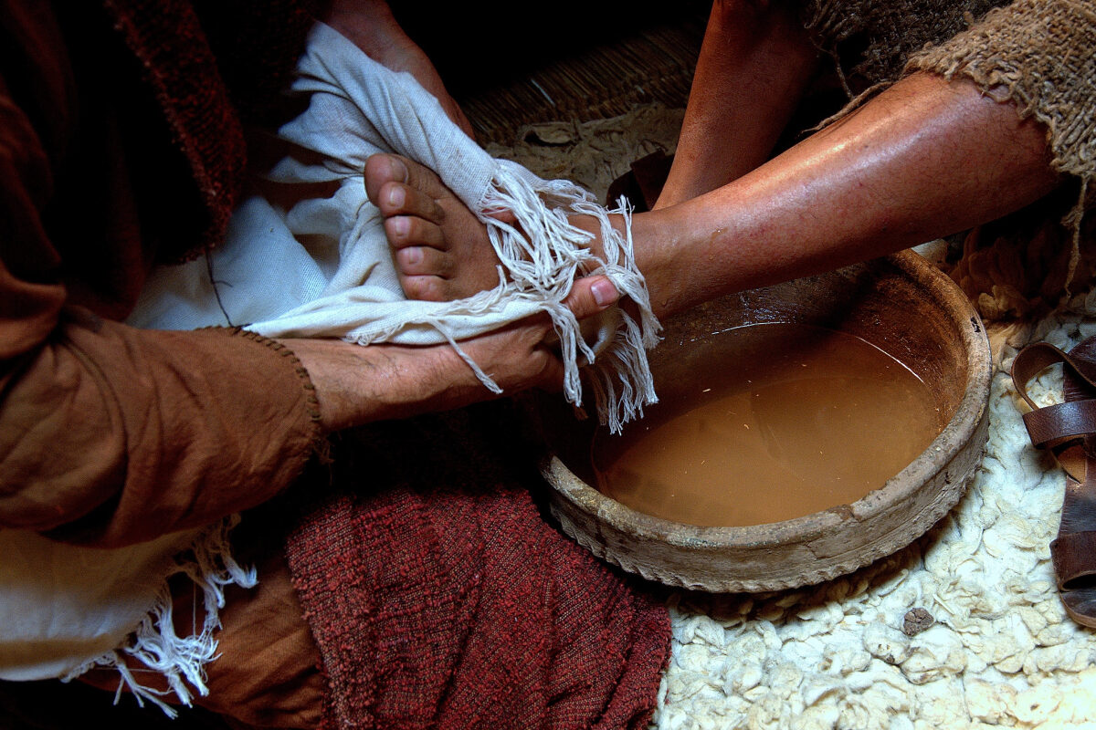 A person gently washes another’s foot with water and cloth, showing an act of humility and care.