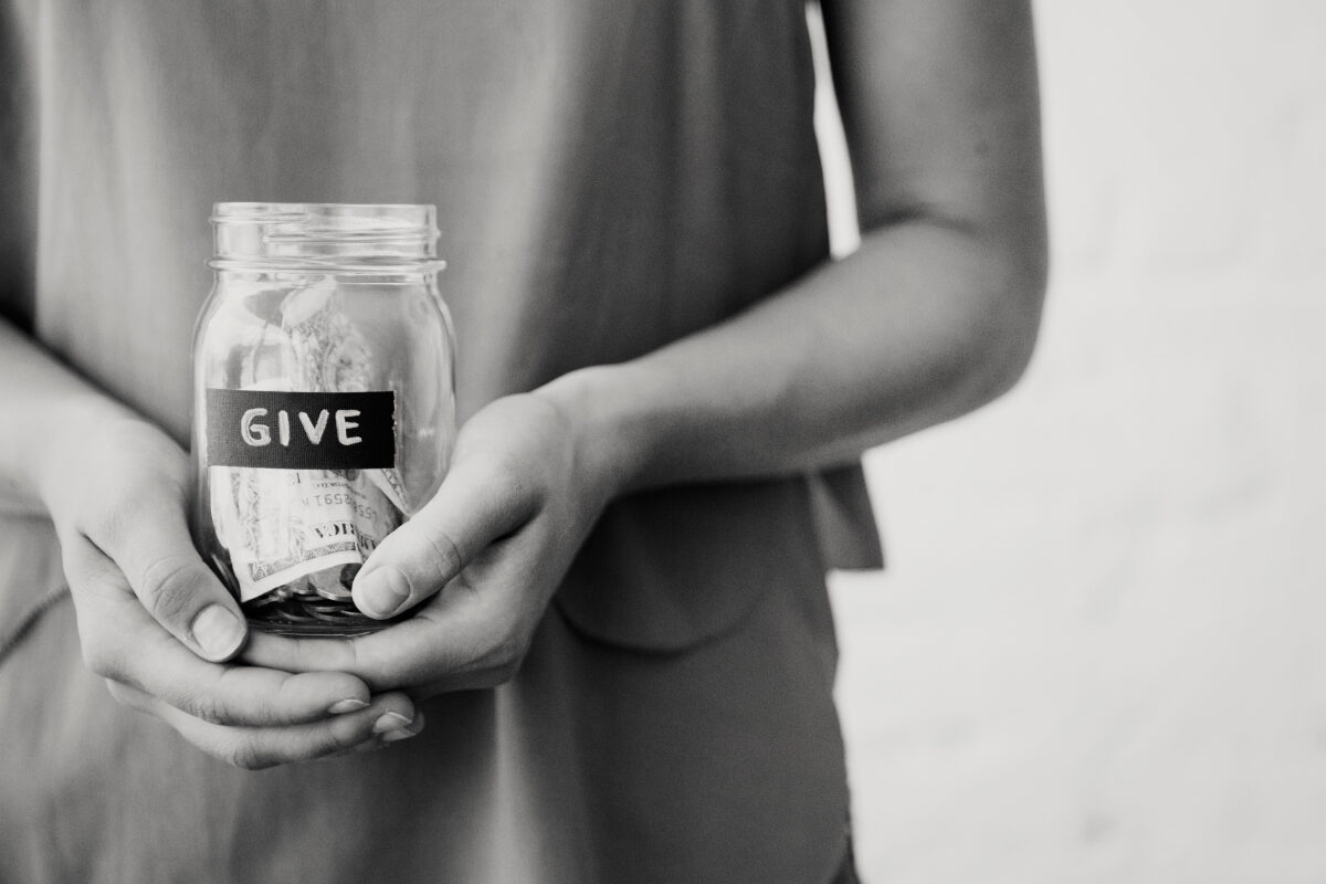 A person holds a jar labeled “give,” filled with money.