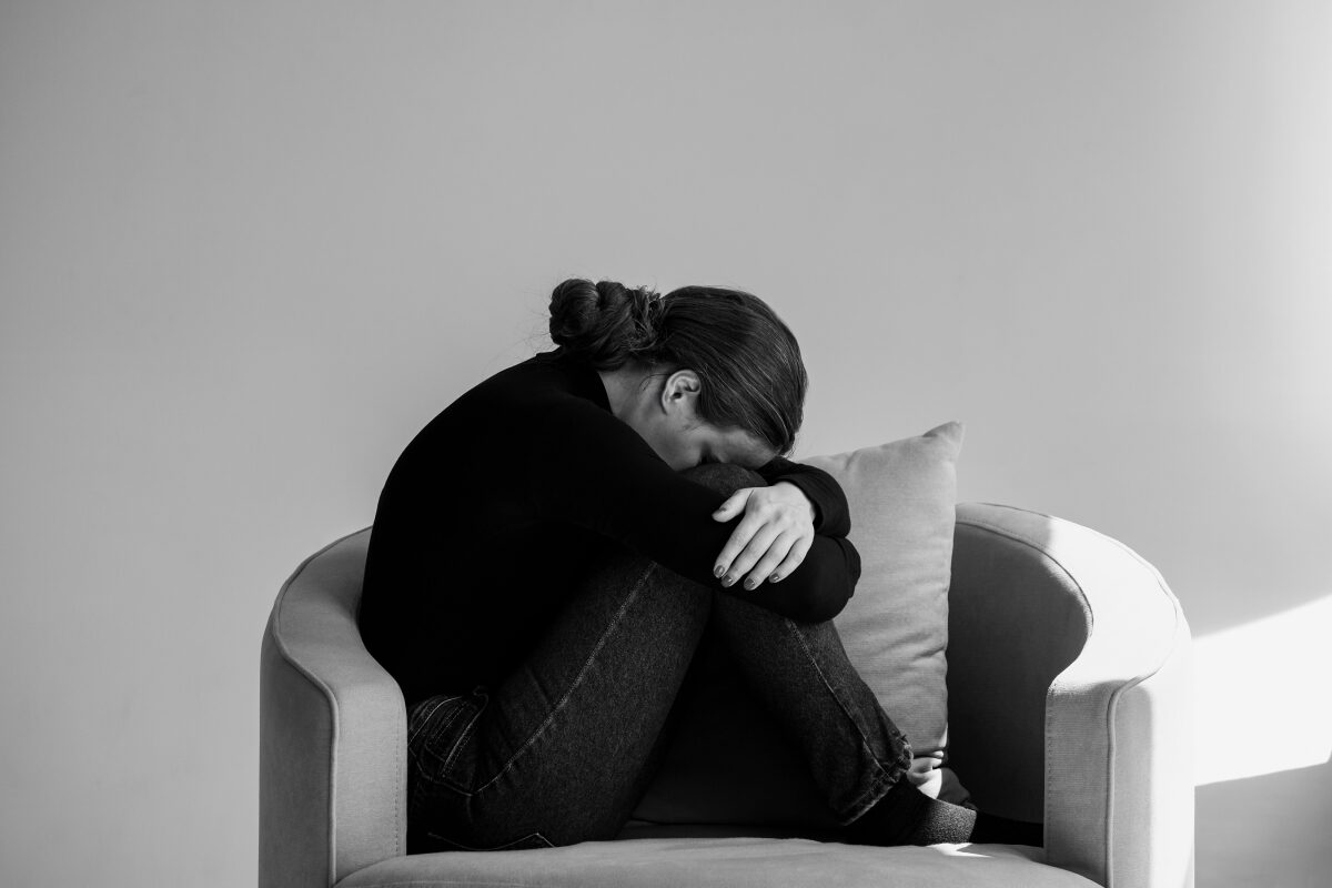 A photo of a woman curled up on a couch, her head resting on her arms in a quiet moment of distress.